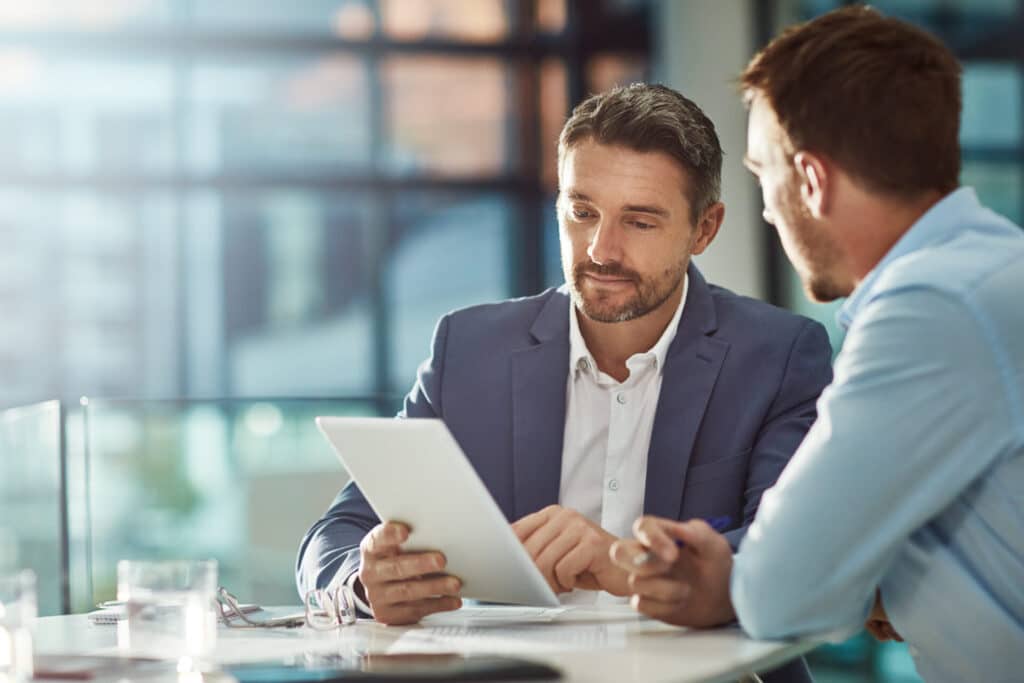 SEO specialist explaining what on-page SEO is to his client while showing him examples on a tablet.